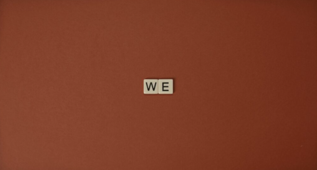 Close-up of Scrabble tiles spelling 'WE' on a brown background, symbolizing unity.